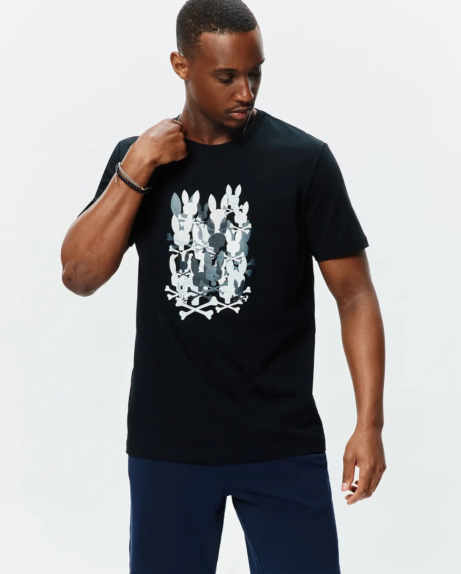 Mens Tanner Graphic Tee, black classic fit jersey t-shirt featuring a large central graphic of stacked white and grey camouflage-patterned Psycho Bunny skull logos with crossbones.