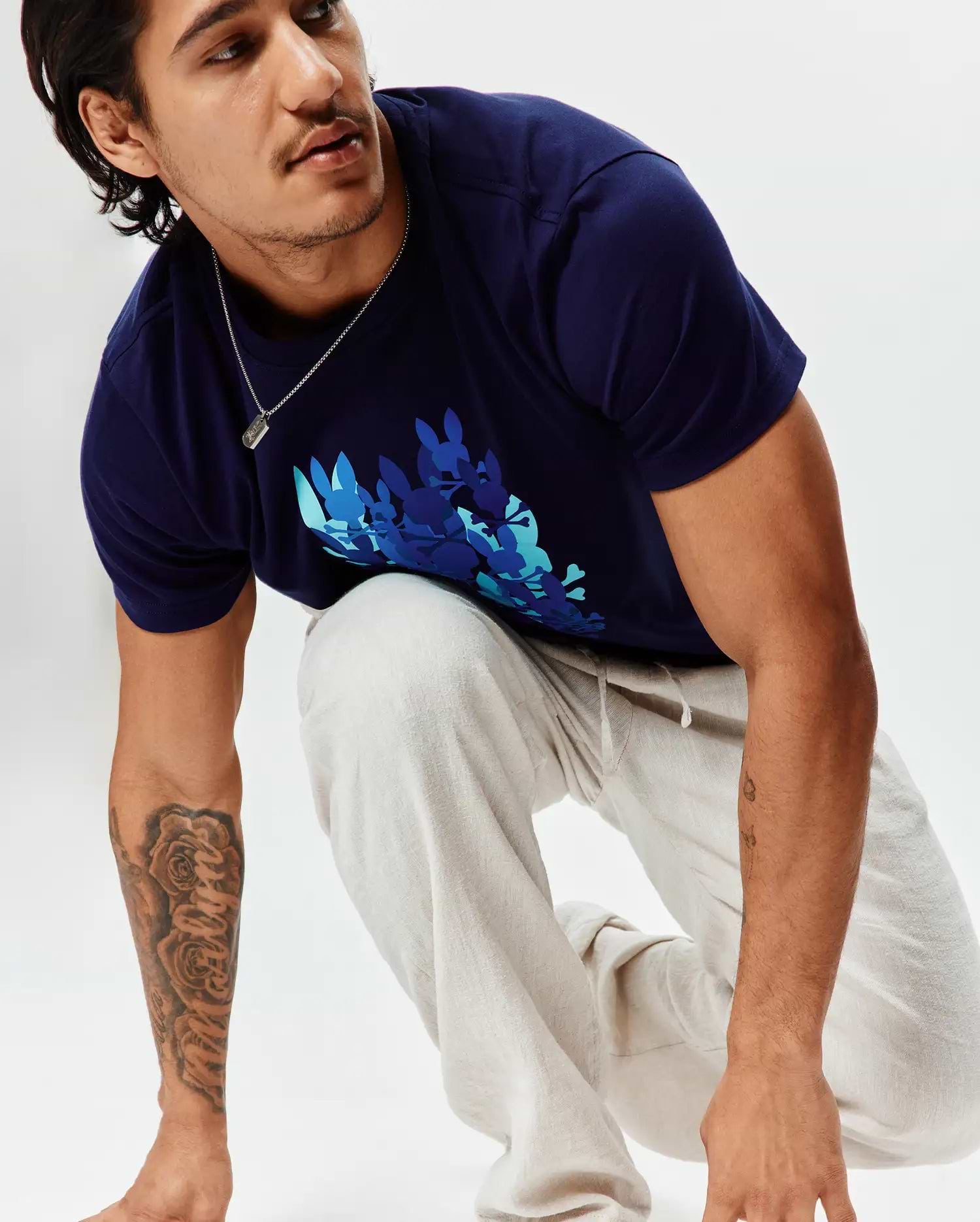 Mens Tanner Graphic Tee, a classic fit navy blue jersey t-shirt with a large chest graphic of multiple bunny skulls in teal, light blue, and darker blue. Paired with light beige textured drawstring pants.