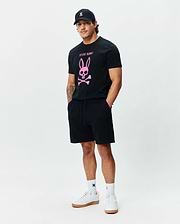 Mens Adler Graphic Tee, a classic fit black jersey t-shirt with a large pink Psycho Bunny skull and crossbones chest graphic. Black French terry shorts, a black cap, and white socks with bunny skull logos. (5)
