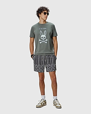 Mens Adler Graphic Tee in olive green jersey with a large white Psycho Bunny skull and crossbones graphic, paired with black and white striped shorts featuring a lower scalloped pattern of small bunny skull logos.