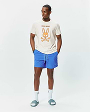 Mens Adler Graphic Tee in cream jersey with a large orange Psycho Bunny skull graphic on the chest, paired with bright blue swim shorts featuring an aqua drawstring and small embroidered logo. (5)