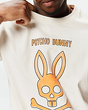 Mens Adler Graphic Tee, a cream, smooth jersey knit t-shirt with a large, bold orange and black outlined Psycho Bunny skull graphic and text prominently displayed on the chest, offering a classic fit. (3)