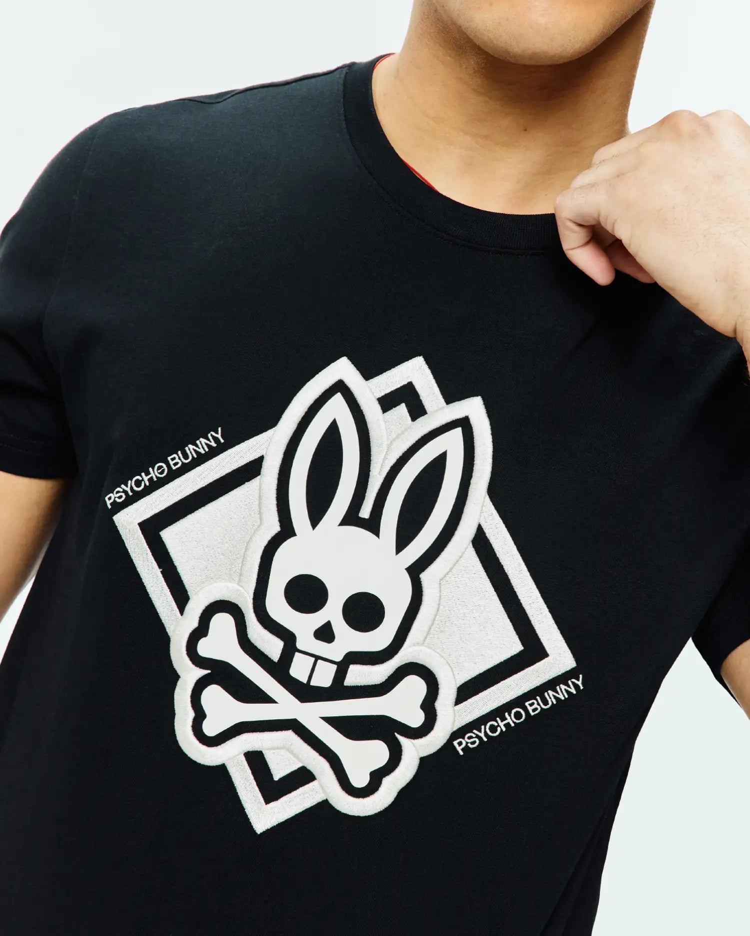 Mens Tobias Graphic Tee, black classic fit jersey t-shirt with a large white embroidered Psycho Bunny skull and crossbones chest logo, with square outline and PSYCHO BUNNY text, red inner collar.