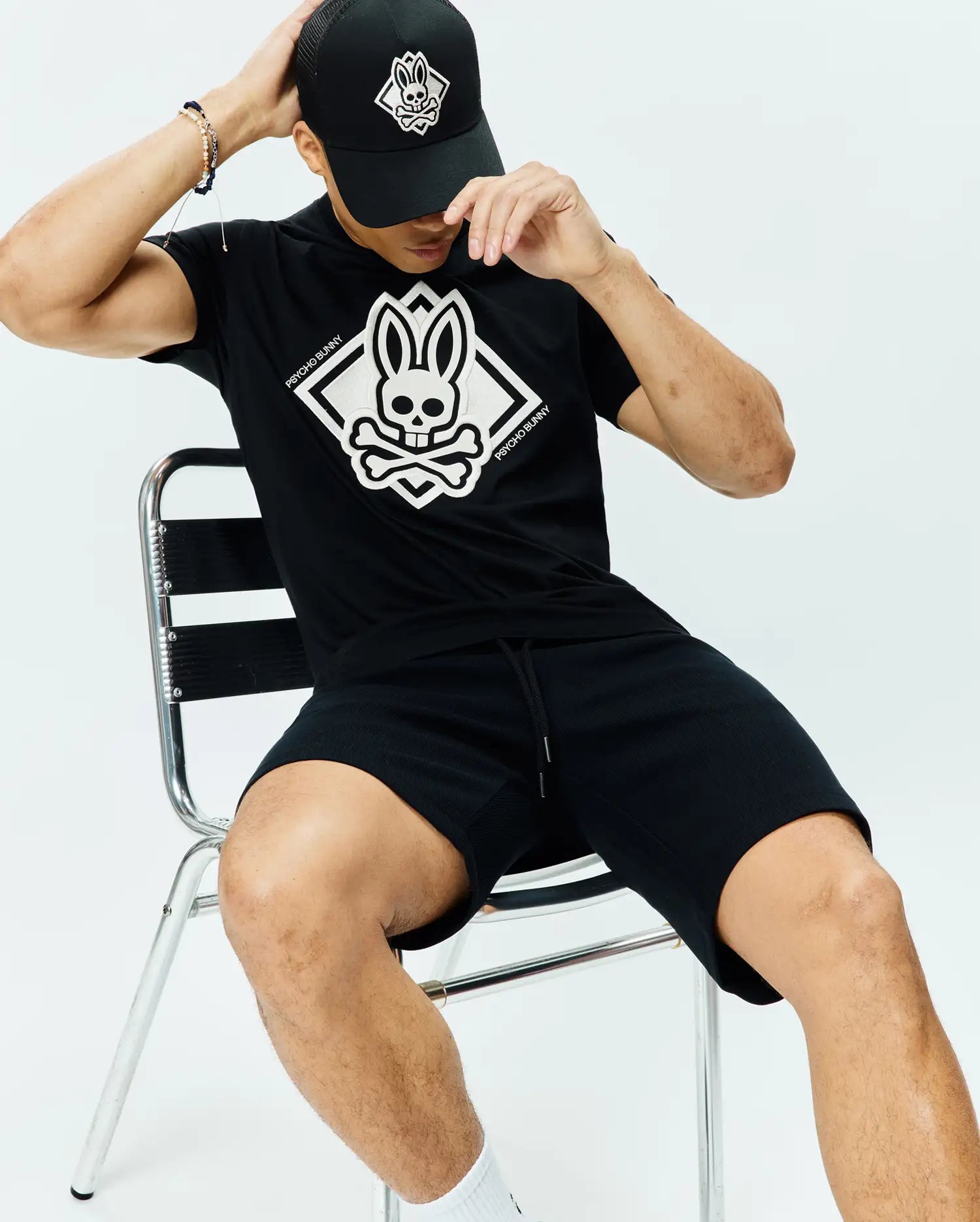 Black Mens Tobias Graphic Tee, classic jersey fit, with a large white Psycho Bunny skull and crossbones diamond chest graphic. Paired with black textured drawstring shorts and a black mesh cap with white logo.