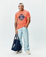 Mens Tobias Graphic Tee, a classic fit coral jersey t-shirt with a large, centered navy blue Psycho Bunny skull logo within a diamond graphic, accented by brand text.