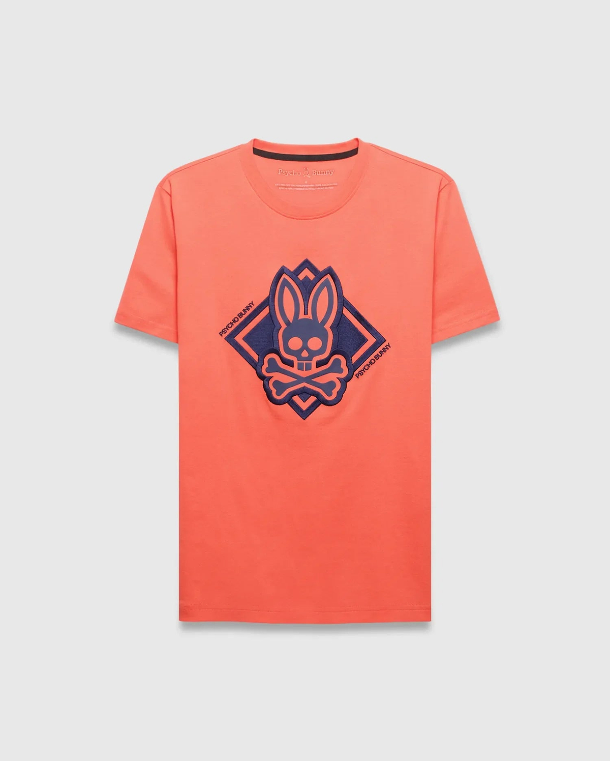 Mens Tobias Graphic Tee, a classic fit coral jersey t-shirt with a large navy blue Psycho Bunny skull and crossbones logo within a diamond graphic on the chest.
