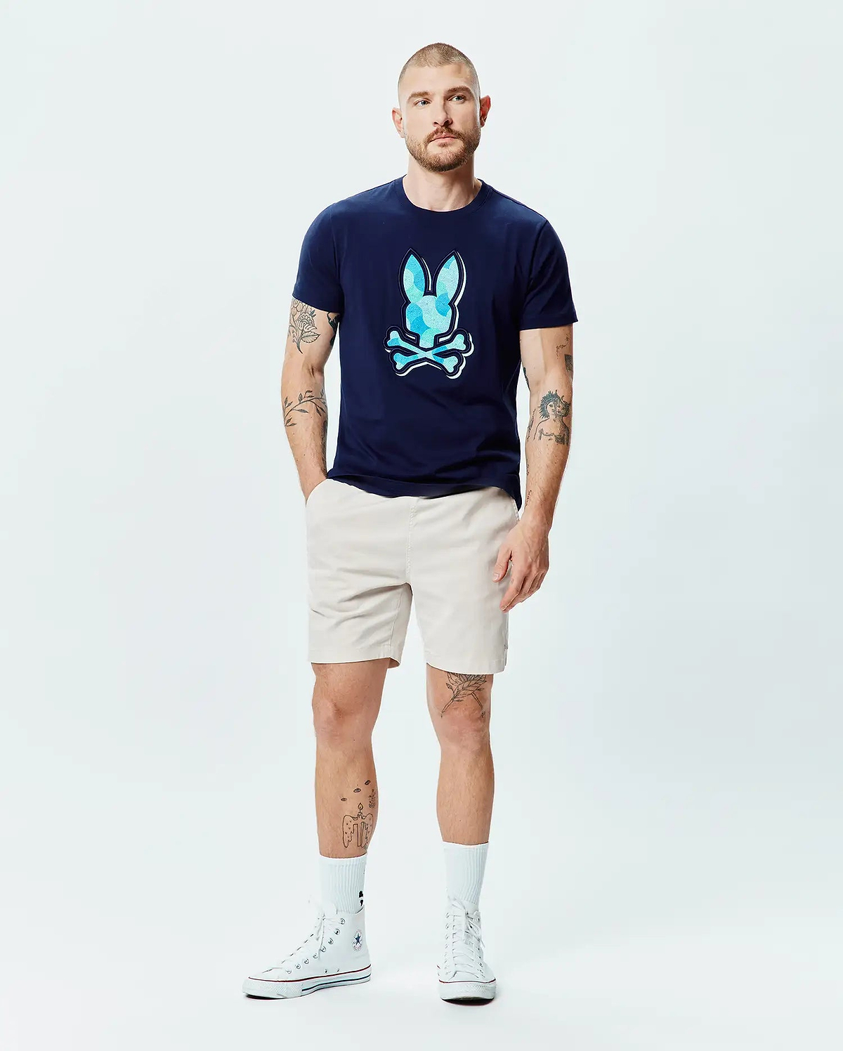 Mens Ethan Graphic Tee in navy blue jersey, featuring a large, classic fit, light blue faceted Psycho Bunny skull logo on the chest, paired with classic beige shorts. (6)