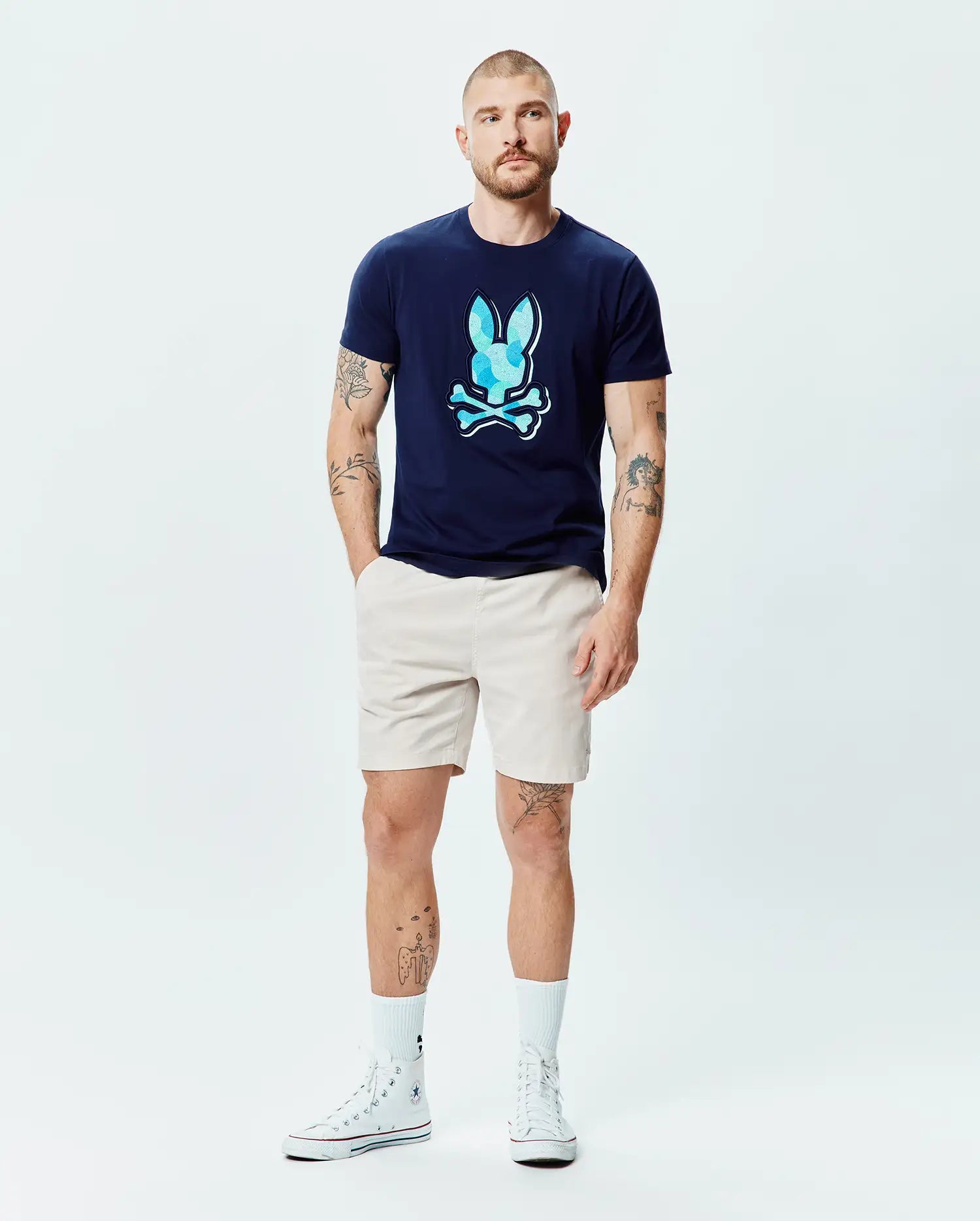 Mens Ethan Graphic Tee in navy blue jersey, featuring a large, classic fit, light blue faceted Psycho Bunny skull logo on the chest, paired with classic beige shorts. (6)