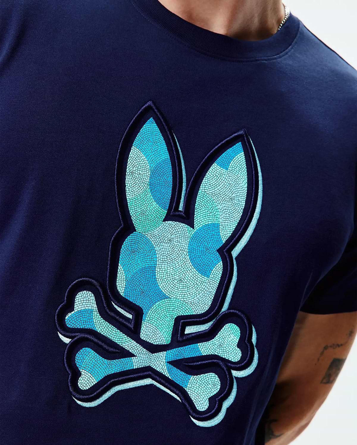 Mens Ethan Graphic Tee. Navy blue jersey t-shirt with a large, textured, mosaic-patterned Psycho Bunny skull logo in shades of blue and teal on the chest, classic fit. (4)
