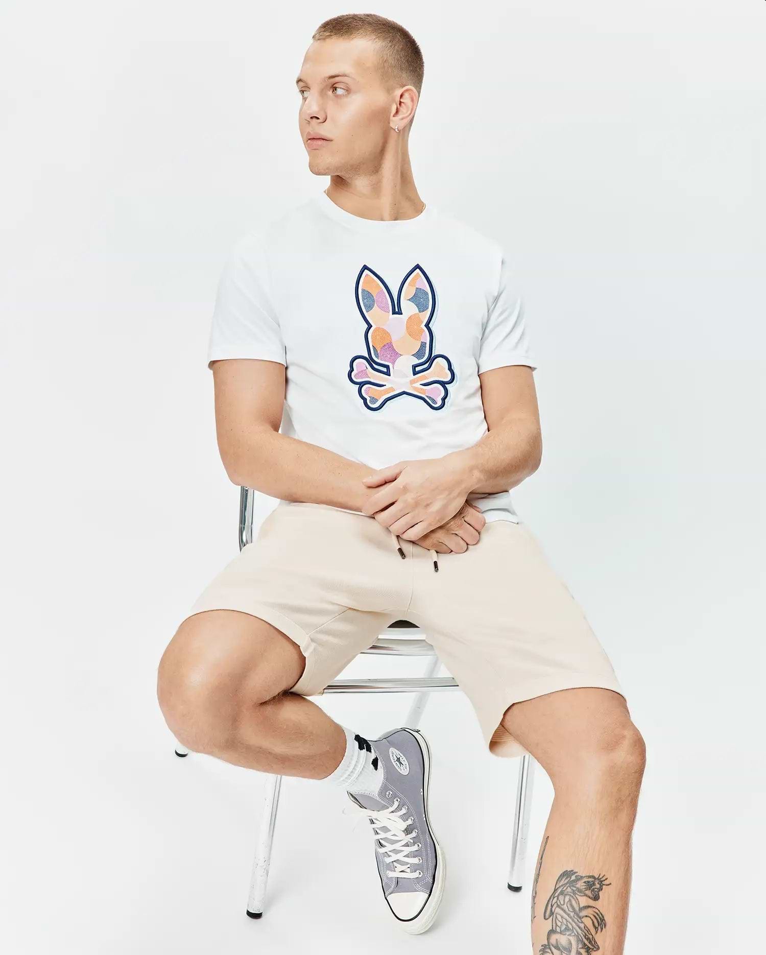 Mens Ethan Graphic Tee, white classic fit jersey with a large colorful mosaic Psycho Bunny skull logo on the chest, paired with relaxed fit beige knit drawstring shorts. (4)