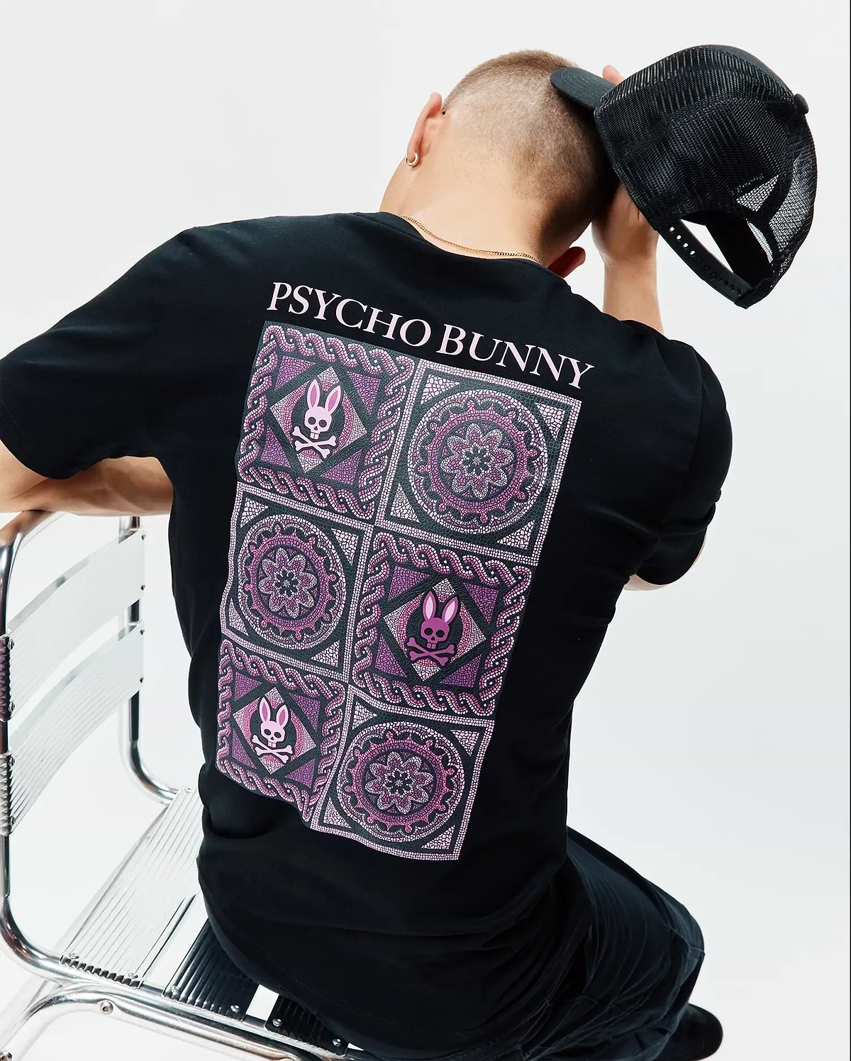 Mens Frank Back Graphic Tee, black classic fit jersey t-shirt with a large back graphic featuring pink and purple mosaic patterns, mandalas, and small Psycho Bunny skull logos, topped with pink PSYCHO BUNNY text.