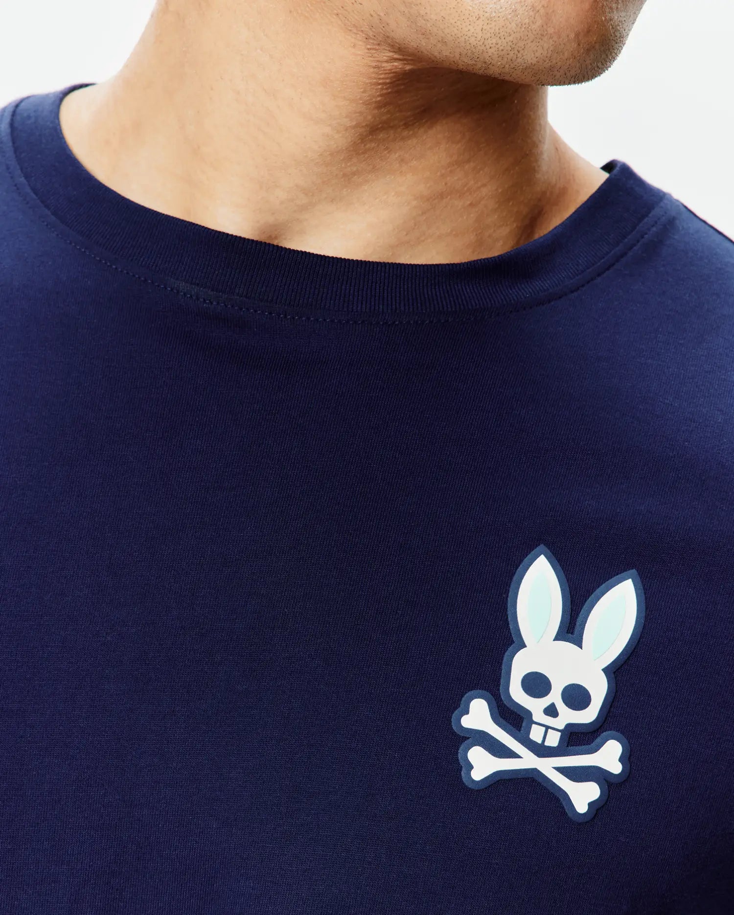 Mens Frank Back Graphic Tee, a navy blue jersey knit t-shirt with a classic fit, featuring a prominent white and light blue Psycho Bunny skull and crossbones appliqué on the left chest.