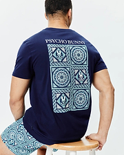 Mens Frank Back Graphic Tee. Navy blue classic fit jersey tee with a large teal, light blue, and white mosaic back graphic featuring Psycho Bunny skull logos and geometric patterns, plus Psycho Bunny text.