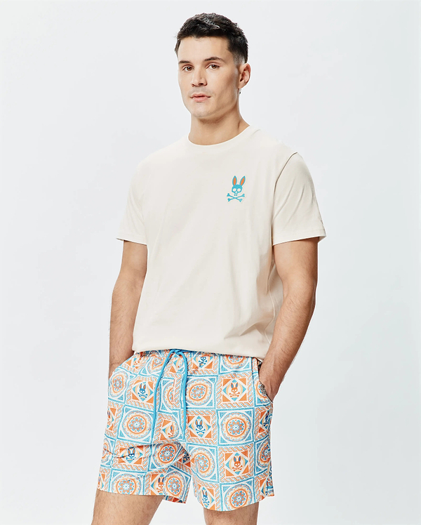 Mens Frank Back Graphic Tee, a cream jersey t-shirt with an embroidered teal/orange Psycho Bunny logo, paired with swim shorts featuring an all-over teal/orange tile print with bunny skull details.
