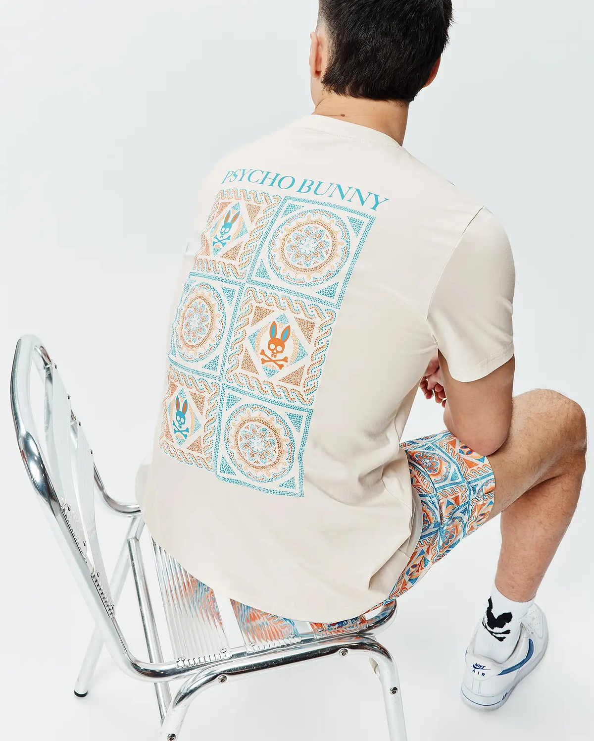Cream classic fit jersey T-shirt with a large back graphic print featuring teal and orange geometric mandala patterns and Psycho Bunny skull logos, plus teal Psycho Bunny text. Mens Frank Back Graphic Tee.