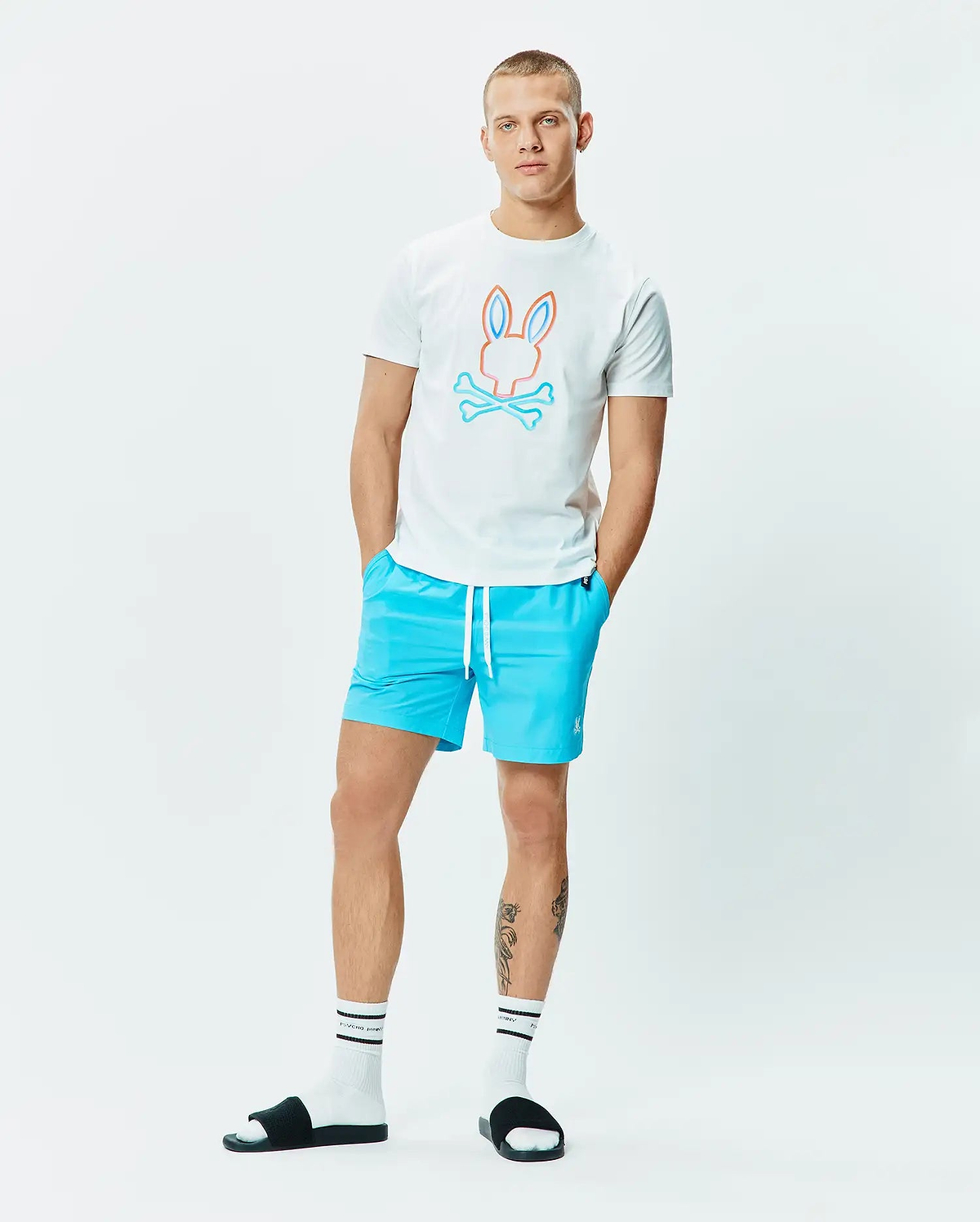 Mens Dayton Graphic Tee, white classic fit jersey knit, featuring a large orange and blue outline Psycho Bunny skull logo on the chest, complemented by bright blue relaxed fit swim shorts with a small white embroidered logo. (5)
