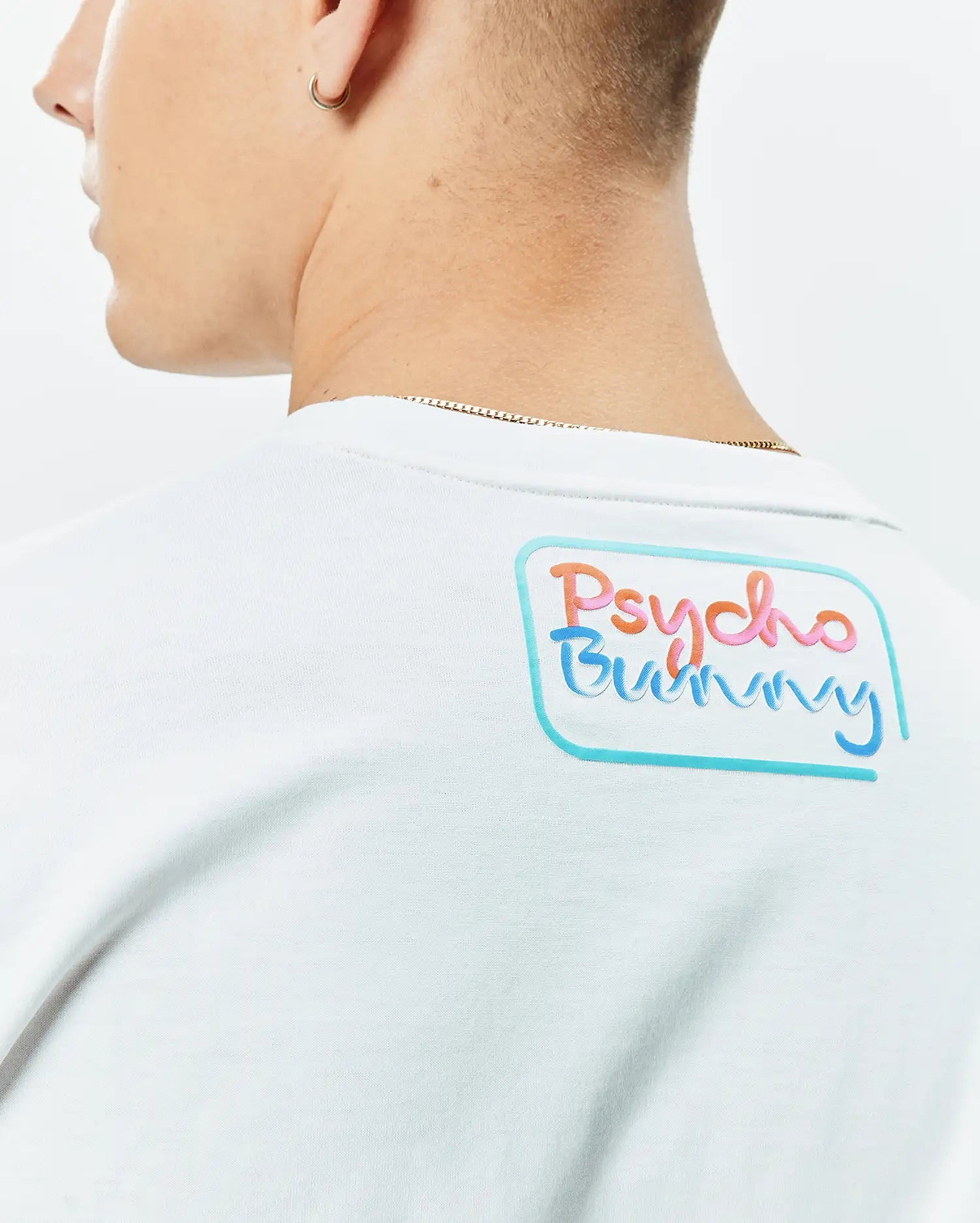 White Mens Dayton Graphic Tee in soft jersey knit, featuring a large, vibrant Psycho Bunny text graphic on the upper back, outlined in light blue. (3)