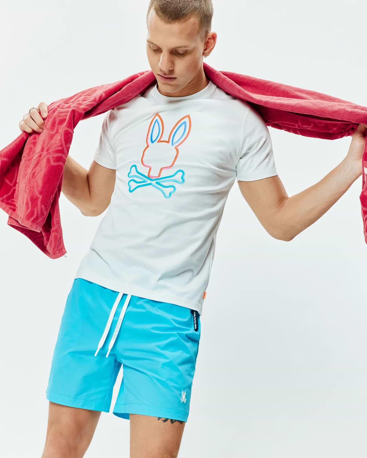 White Mens Dayton Graphic Tee, classic fit jersey, featuring a large orange and blue Psycho Bunny skull logo on the chest, paired with bright blue swim shorts with a small embroidered bunny logo. (4)