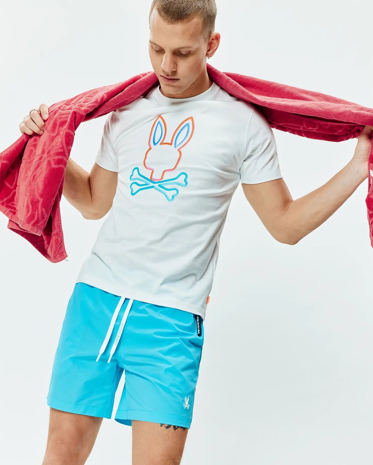 White Mens Dayton Graphic Tee, classic fit jersey, featuring a large orange and blue Psycho Bunny skull logo on the chest, paired with bright blue swim shorts with a small embroidered bunny logo. (4)