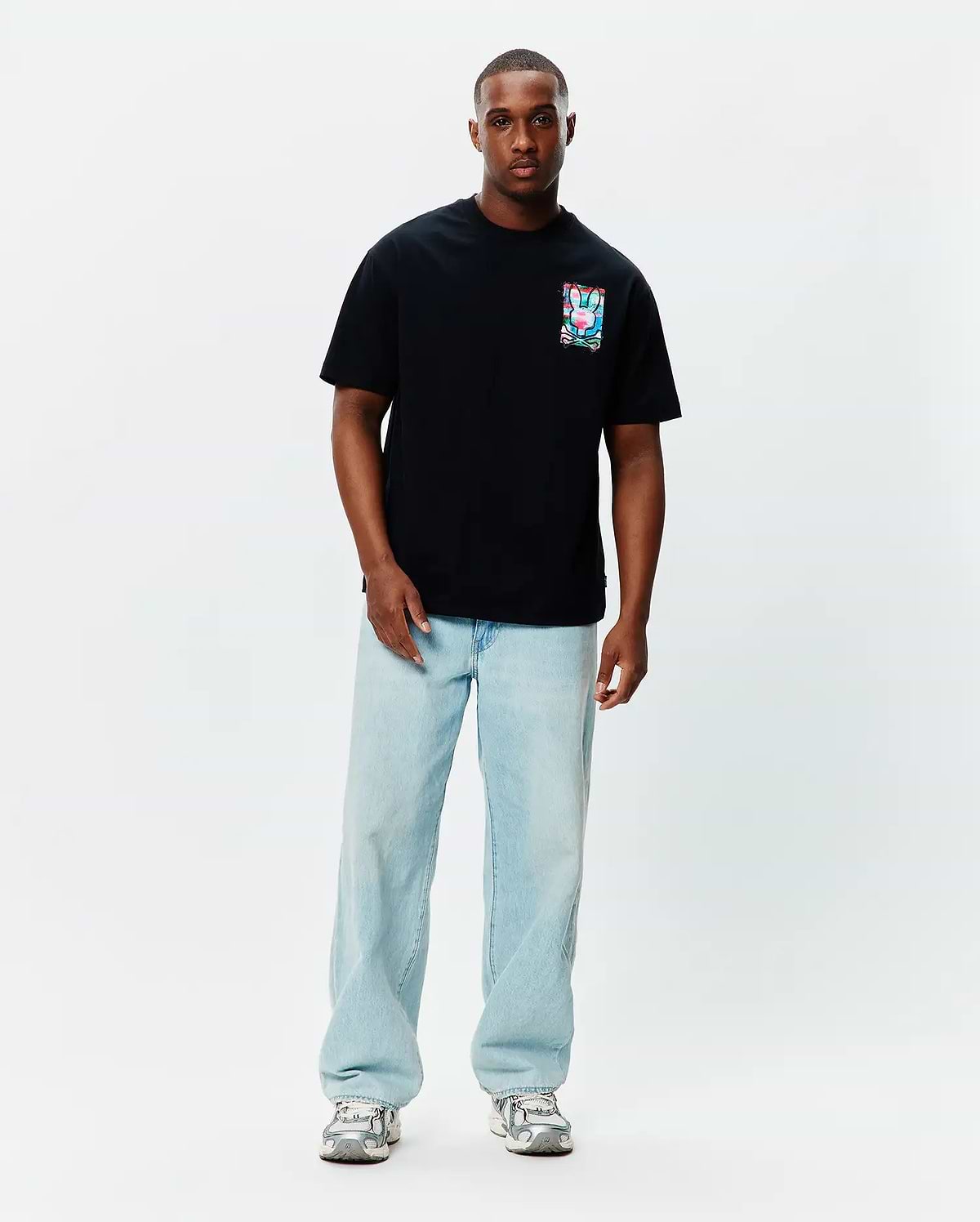 Black Mens Isaac Relaxed Fit Tee, a soft jersey t-shirt featuring a small, square, vibrant multi-color Psycho Bunny skull graphic on the left chest.