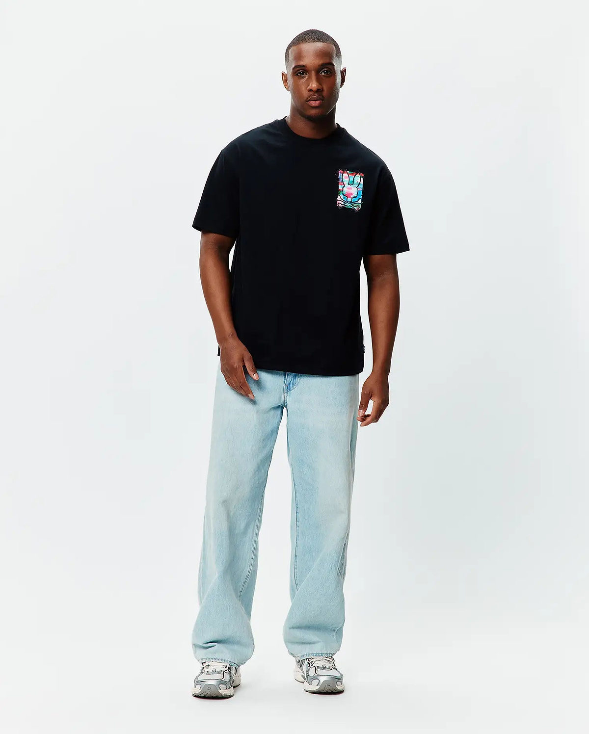 Black Mens Isaac Relaxed Fit Tee, a soft jersey t-shirt featuring a small, square, vibrant multi-color Psycho Bunny skull graphic on the left chest.