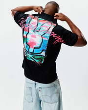 Mens Isaac Relaxed Fit Tee, black jersey with a large, vibrant paint-splatter Psycho Bunny skull graphic in pink, blue, green, and white on the back, featuring a pink Psycho Bunny script logo.