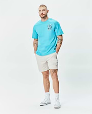 Mens Isaac Relaxed Fit Tee in aqua blue jersey, featuring a blue and white graphic print on the left chest, paired with light beige relaxed shorts with a small embroidered Psycho Bunny logo on the left thigh.