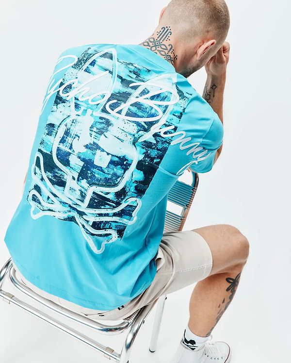 Mens Isaac Relaxed Fit Tee in bright blue jersey, featuring a large abstract brushstroke Psycho Bunny skull graphic in dark blue and white on the back, with white script branding on the back and sleeve.