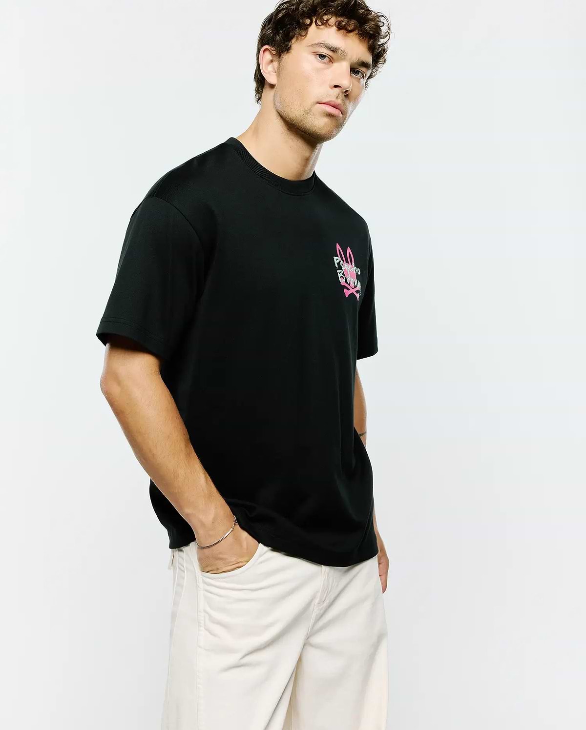 Mens Duncan Relaxed Fit Tee, black jersey knit with a relaxed fit, featuring a prominent pink and white Psycho Bunny skull and crossbones logo on the left chest.