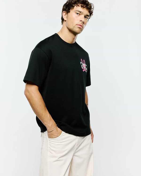 Mens Duncan Relaxed Fit Tee, black jersey knit with a relaxed fit, featuring a prominent pink and white Psycho Bunny skull and crossbones logo on the left chest.