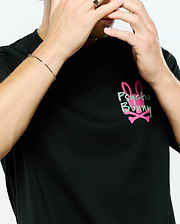MENS DUNCAN RELAXED FIT TEE, a black jersey knit t-shirt featuring a large, distressed light green Psycho Bunny text graphic over a solid pink bunny skull and crossbones logo on the chest.