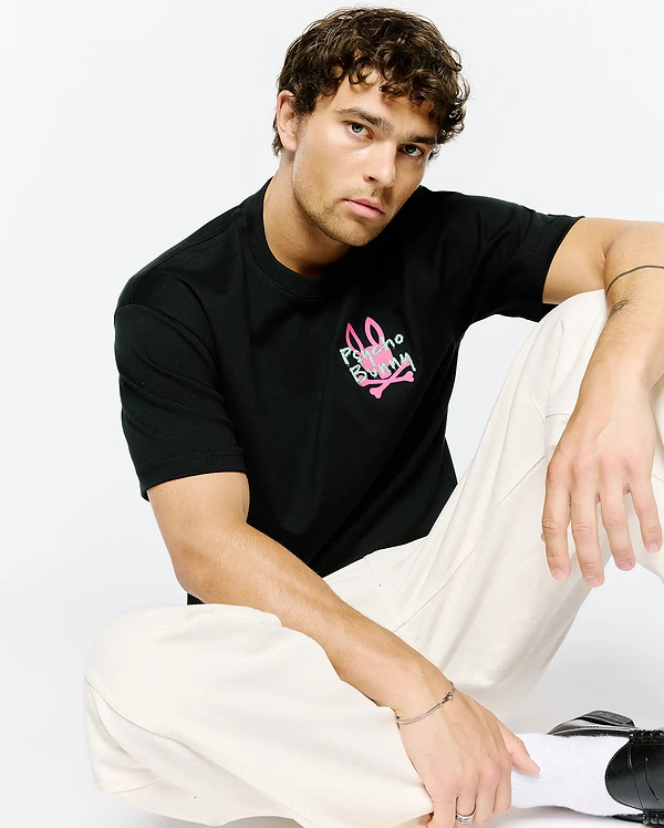 Mens Duncan Relaxed Fit Tee, a black jersey t-shirt with a relaxed fit, featuring a vibrant neon pink and light green Psycho Bunny skull logo graphic print on the chest.