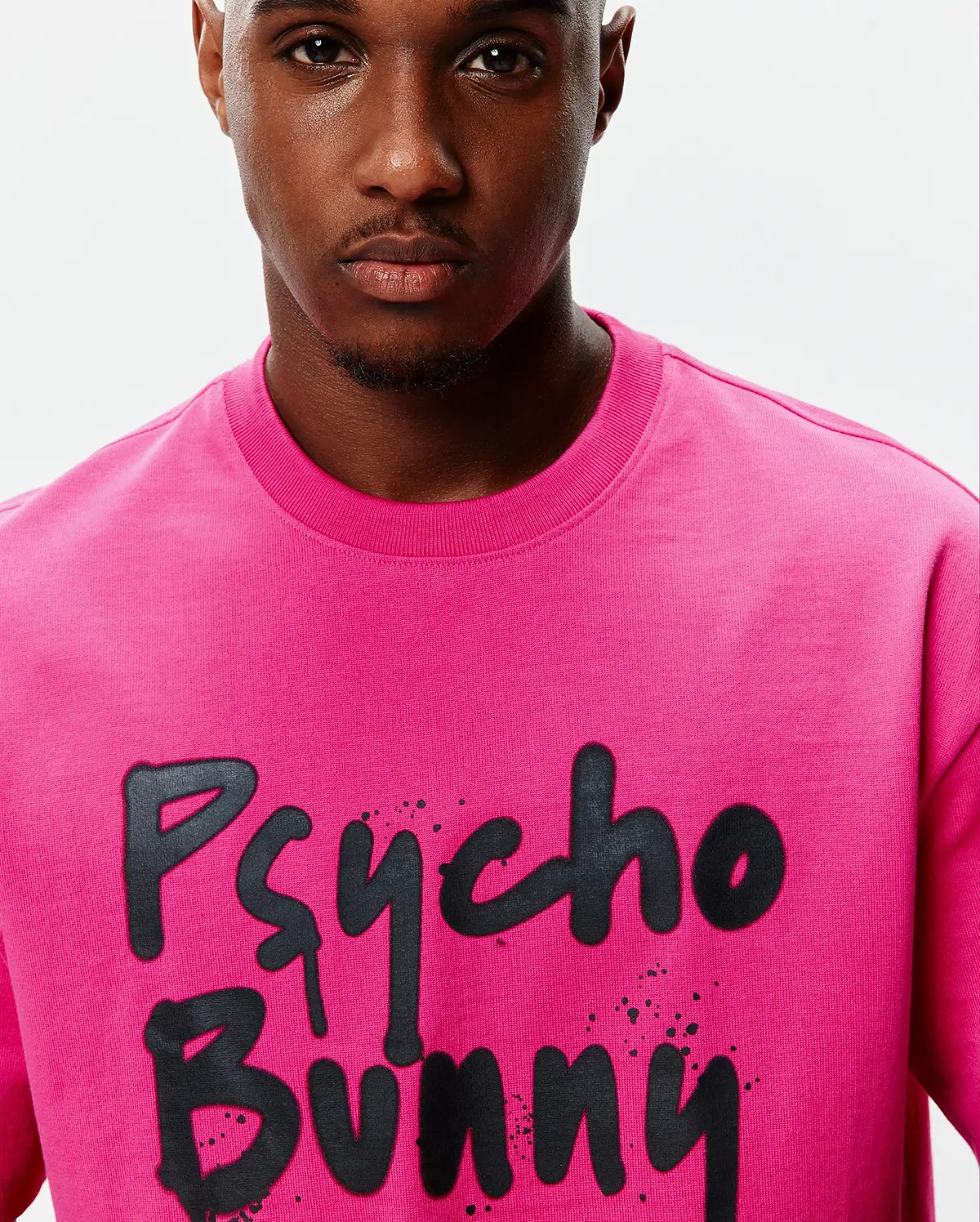 Mens Duncan Wordmark Relaxed Fit Tee in vibrant fuchsia jersey, featuring a large black graffiti-style Psycho Bunny wordmark graphic with splatter details on the chest.