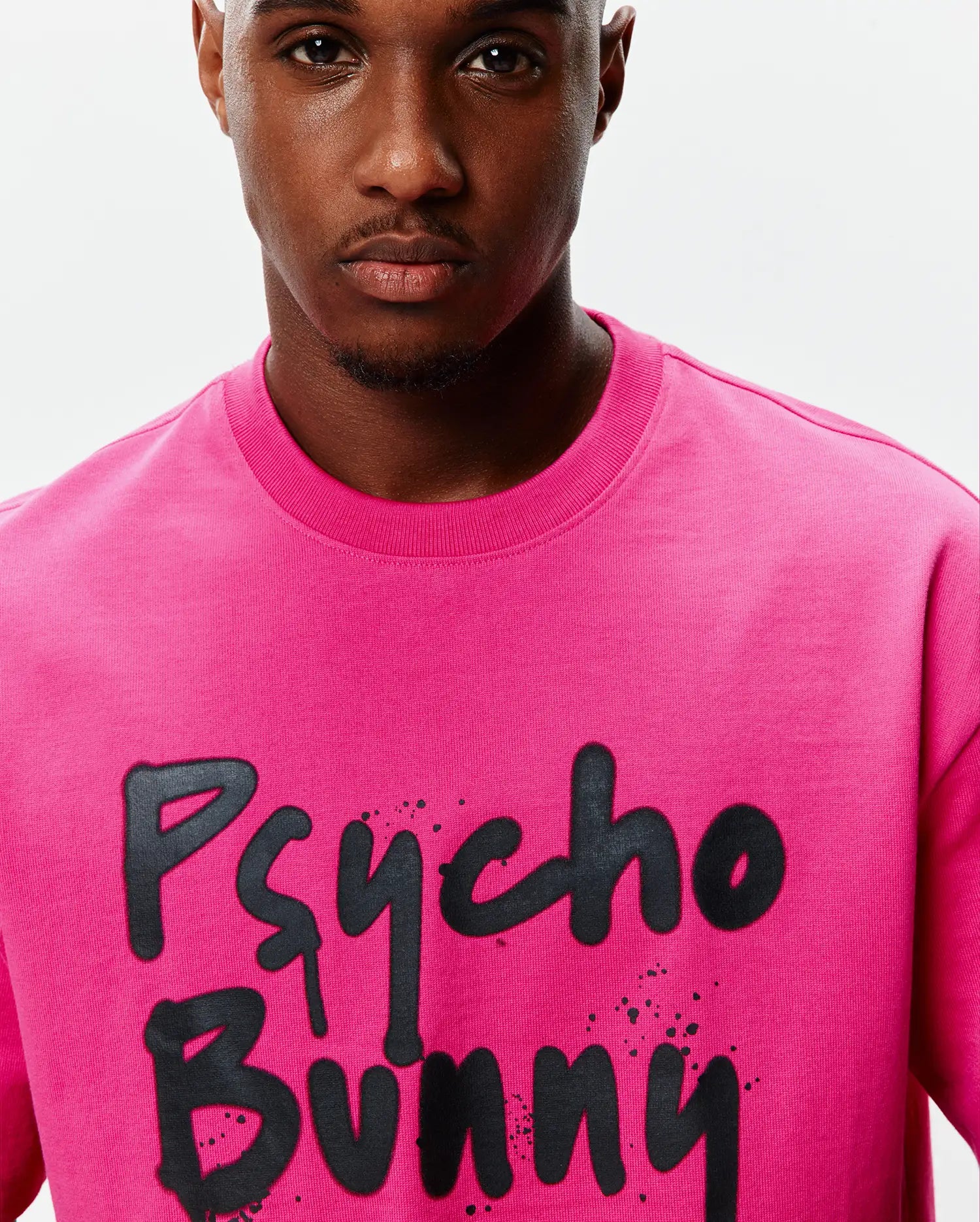 Mens Duncan Wordmark Relaxed Fit Tee in vibrant fuchsia jersey, featuring a large black graffiti-style Psycho Bunny wordmark graphic with splatter details on the chest.