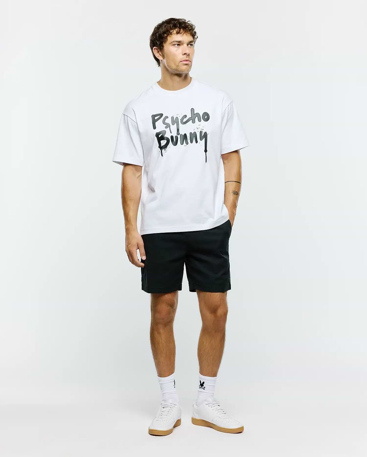 White Mens Duncan Wordmark Relaxed Fit Tee in jersey fabric, featuring a large black and grey graffiti-style Psycho Bunny wordmark with splatter and drip effects on the chest.