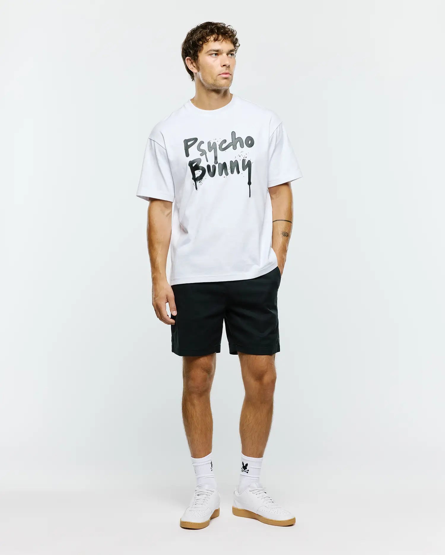 White Mens Duncan Wordmark Relaxed Fit Tee in jersey fabric, featuring a large black and grey graffiti-style Psycho Bunny wordmark with splatter and drip effects on the chest.