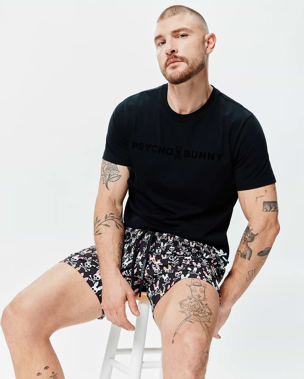 Mens Royce Graphic Tee, a black classic-fit jersey t-shirt with a large tonal PSYCHO BUNNY chest logo, paired with black multi-color all-over bunny skull and crossbones print shorts. (5)