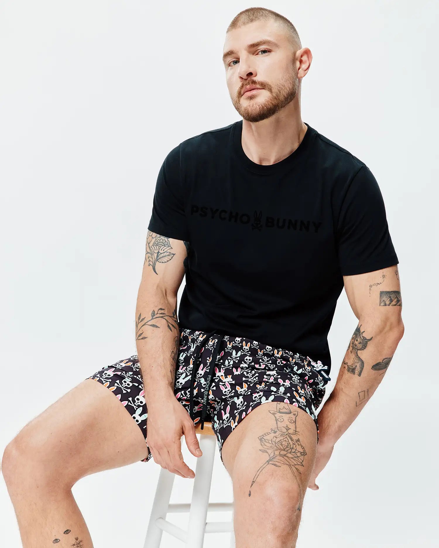 Mens Royce Graphic Tee, a black classic-fit jersey t-shirt with a large tonal PSYCHO BUNNY chest logo, paired with black multi-color all-over bunny skull and crossbones print shorts. (5)