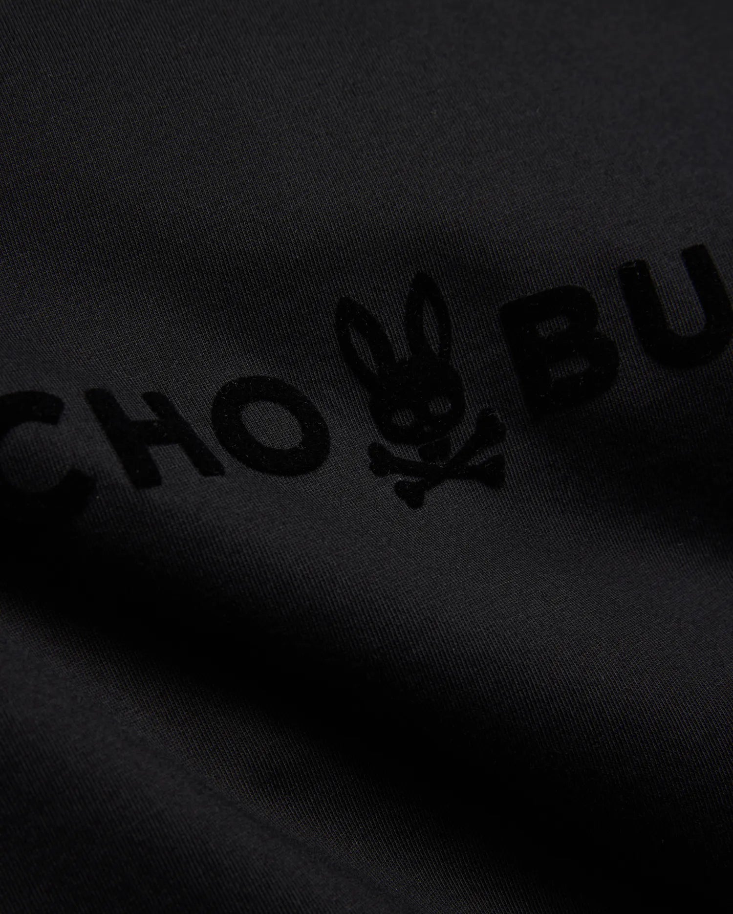 Mens Royce Graphic Tee, a black jersey knit t-shirt with a large, subtly raised, tonal black flocked Psycho Bunny skull logo and brand name graphic. (6)