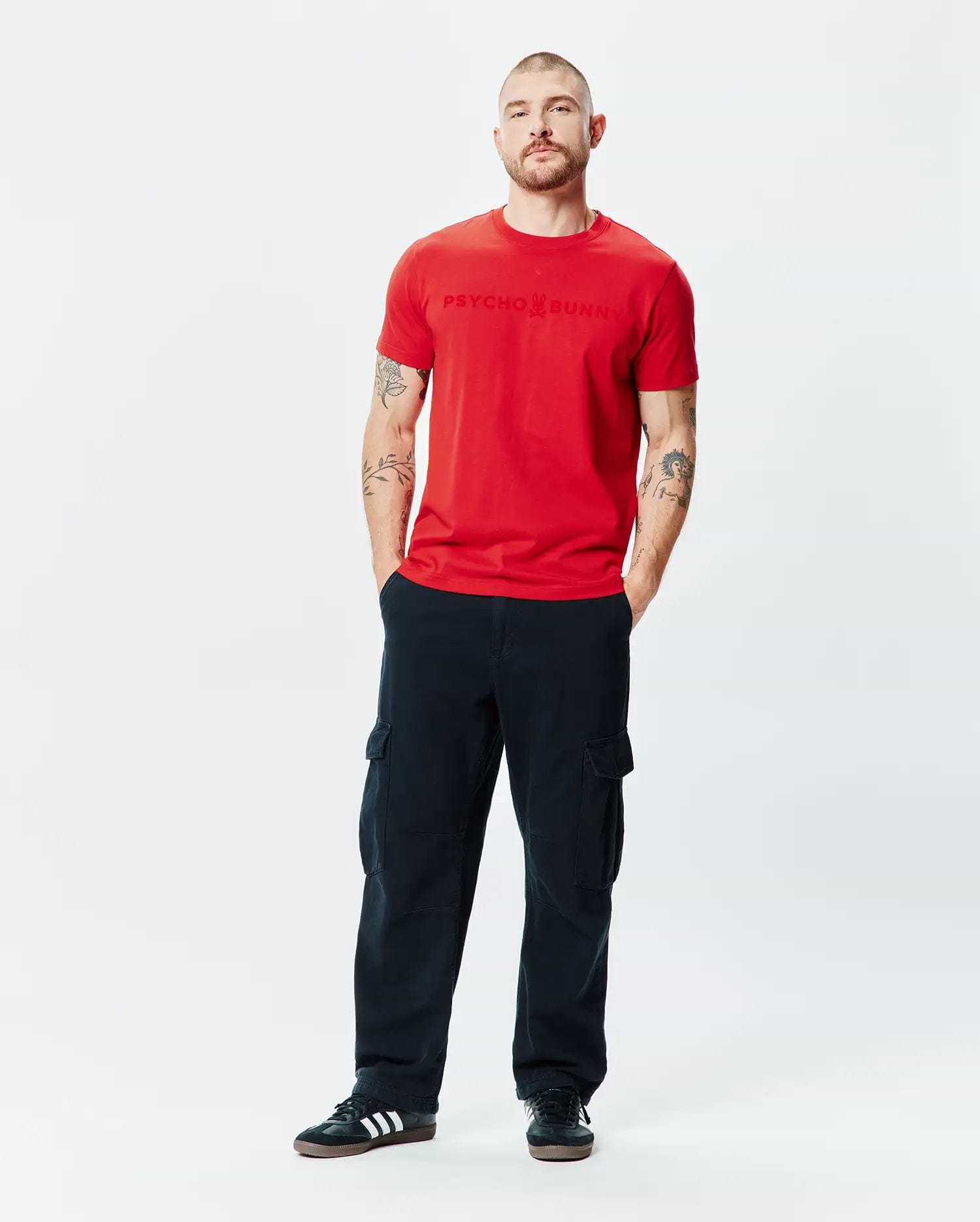 Mens Royce Graphic Tee, a vibrant red classic fit jersey t-shirt featuring a prominent, tonal embossed Psycho Bunny logo text centered on the chest.