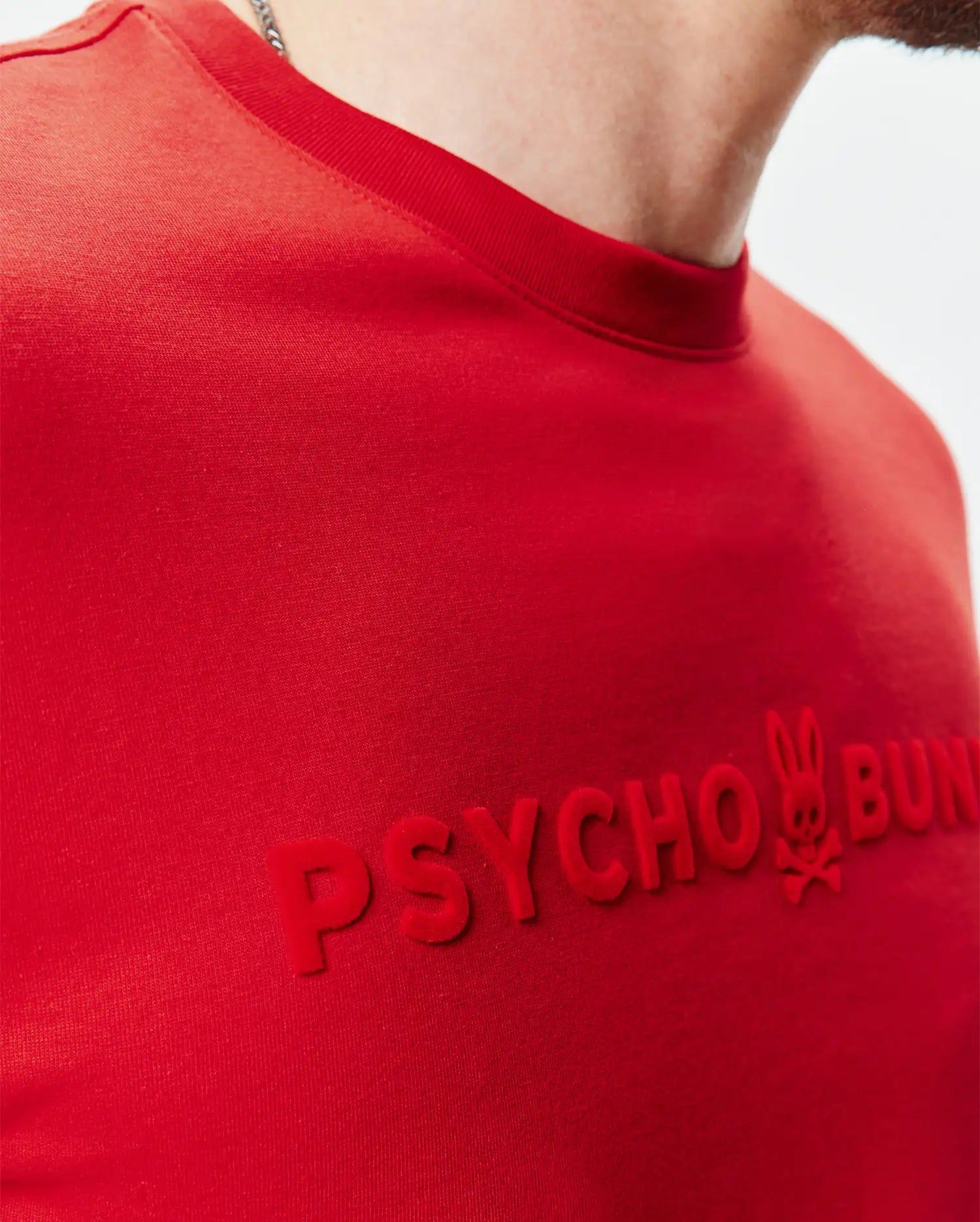 Mens Royce Graphic Tee, a classic fit red jersey knit t-shirt with a large, raised, velvety red PSYCHO BUNNY text graphic and iconic bunny skull logo on the chest.