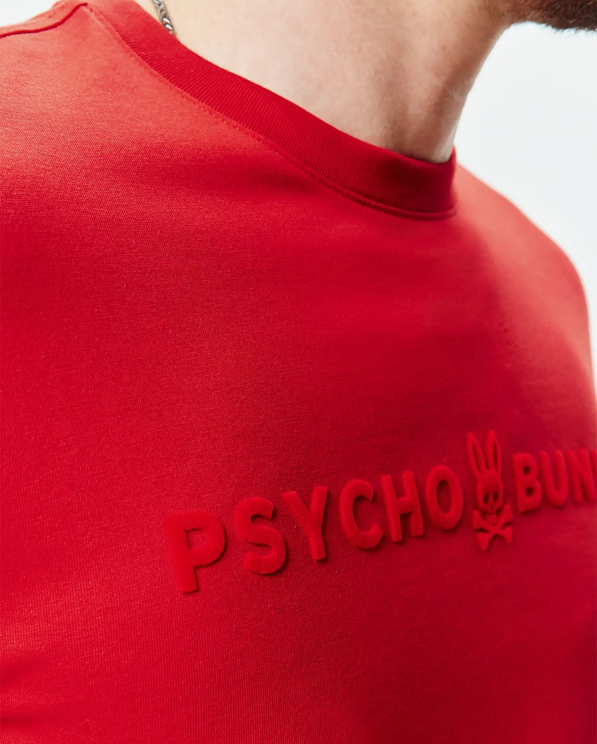 Mens Royce Graphic Tee, a classic fit red jersey knit t-shirt with a large, raised, velvety red PSYCHO BUNNY text graphic and iconic bunny skull logo on the chest.
