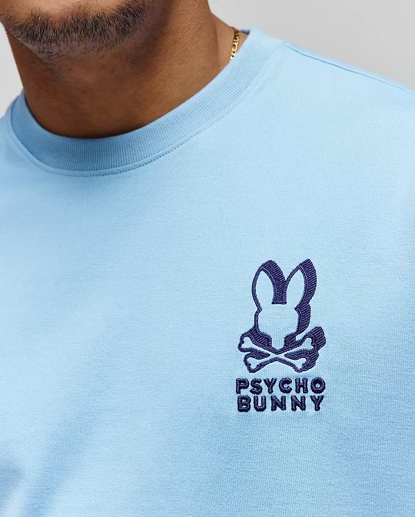 Mens Toby Oversized Tee in light blue jersey knit, featuring a prominent dark blue embroidered Psycho Bunny skull logo with text on the left chest. (2)