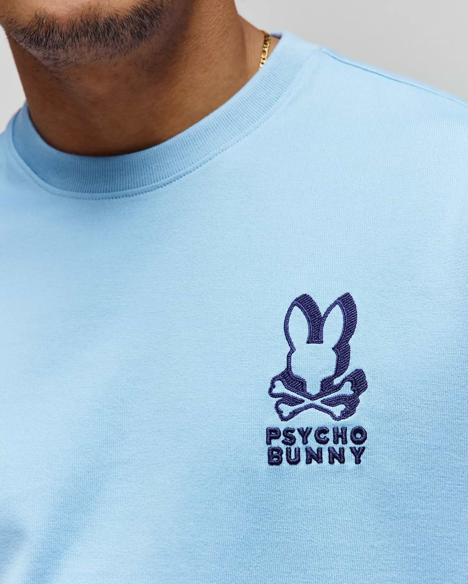 Mens Toby Oversized Tee in light blue jersey knit, featuring a prominent dark blue embroidered Psycho Bunny skull logo with text on the left chest. (2)