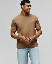 Mens Maxton Waffle Tee in tan, featuring a classic fit and textured waffle knit fabric. A small, embroidered Psycho Bunny skull logo in white, blue, and black adorns the left chest.