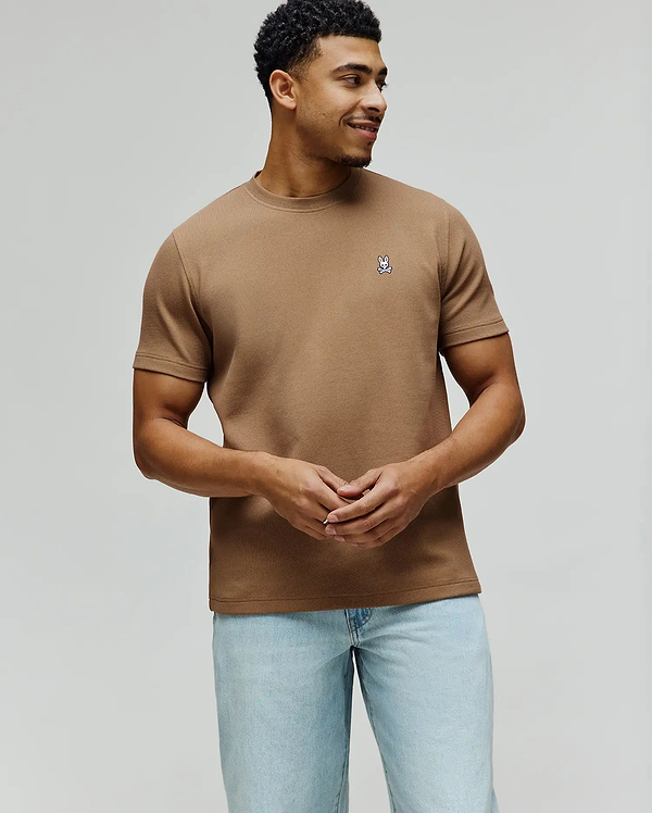 Mens Maxton Waffle Tee in tan, featuring a classic fit and textured waffle knit fabric. A small, embroidered Psycho Bunny skull logo in white, blue, and black adorns the left chest.