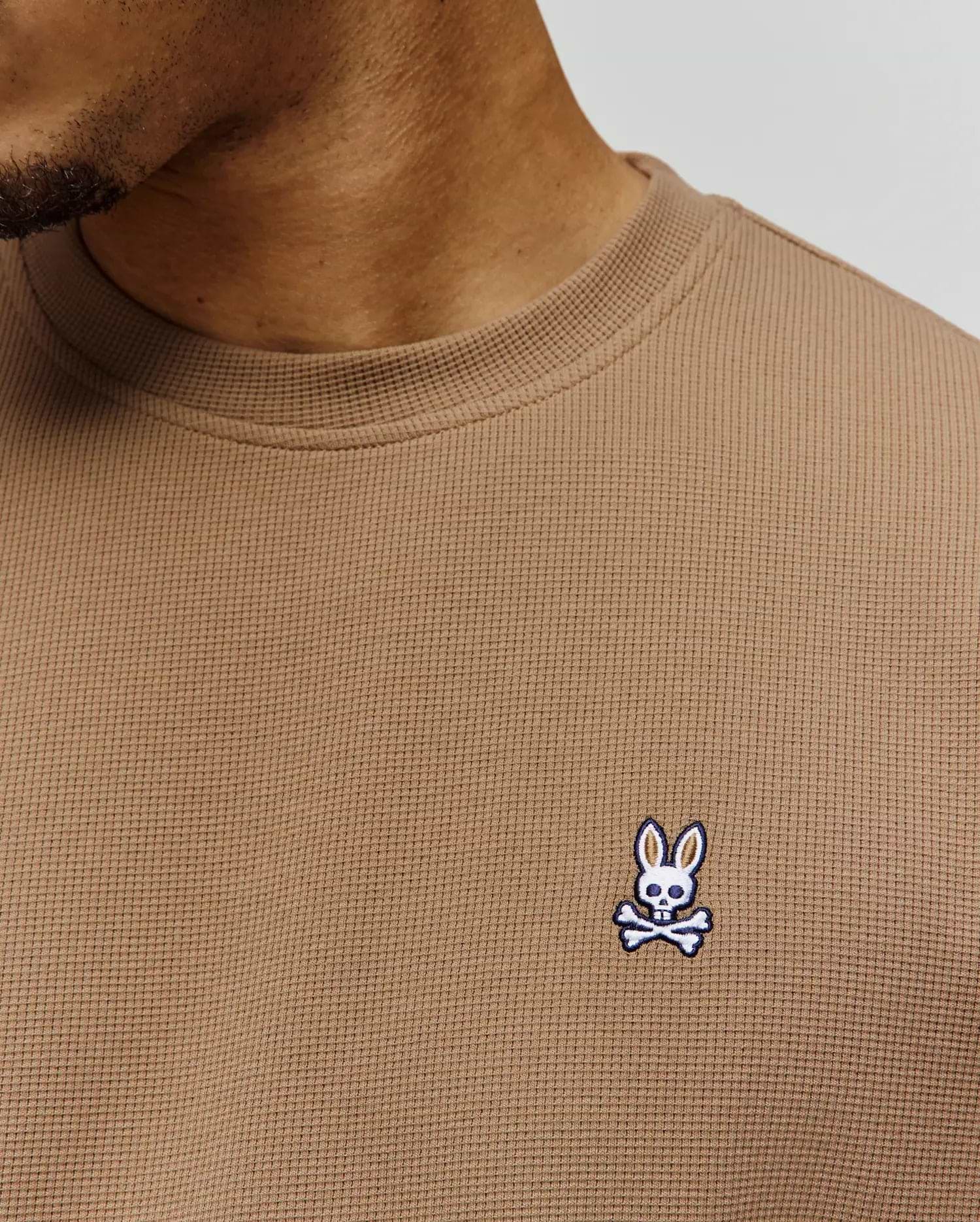 Mens Maxton Waffle Tee in tan, featuring a classic fit and textured waffle knit fabric. A small, embroidered Psycho Bunny skull logo in white, blue, and black adorns the left chest.