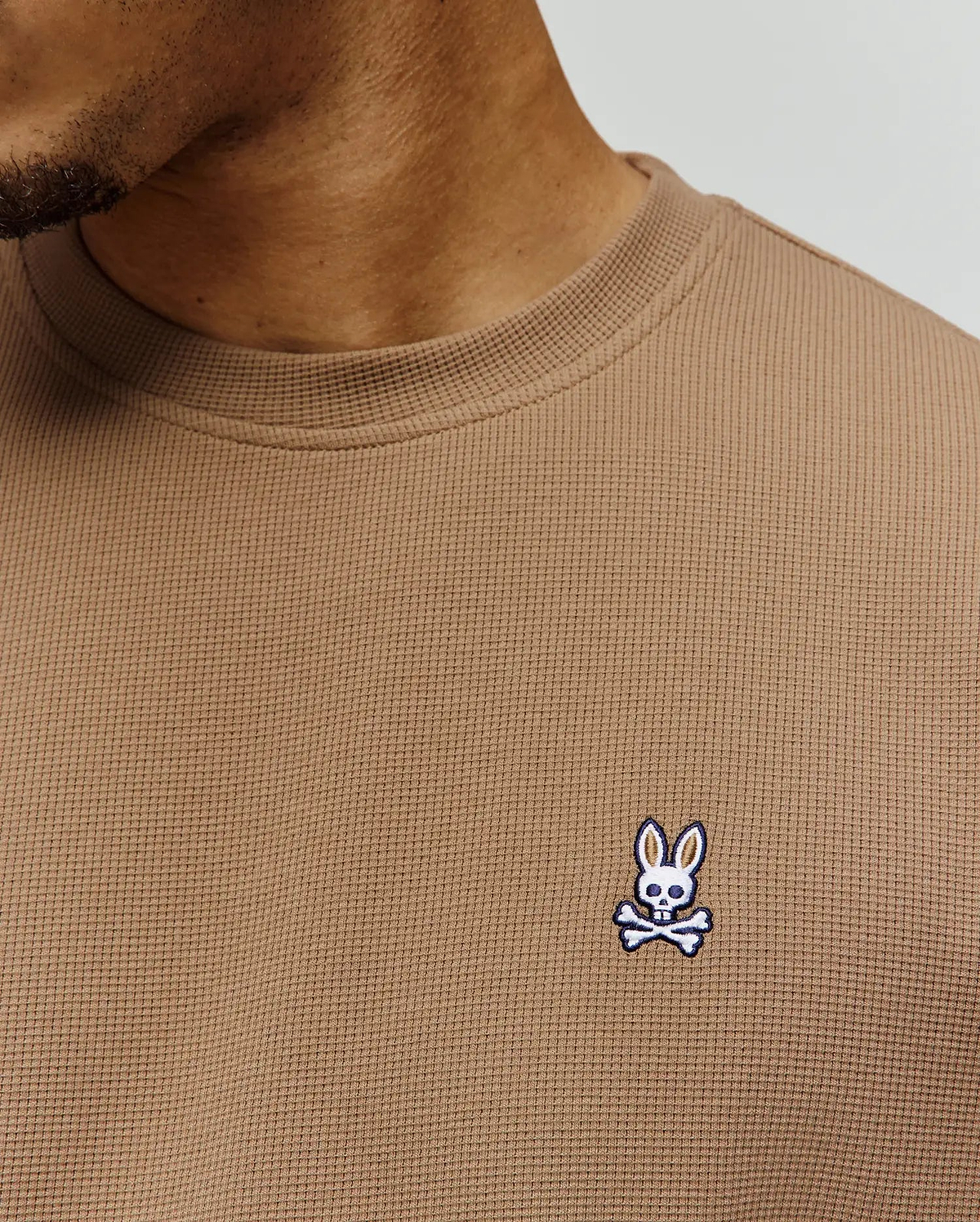 Mens Maxton Waffle Tee in tan, featuring a classic fit and textured waffle knit fabric. A small, embroidered Psycho Bunny skull logo in white, blue, and black adorns the left chest.