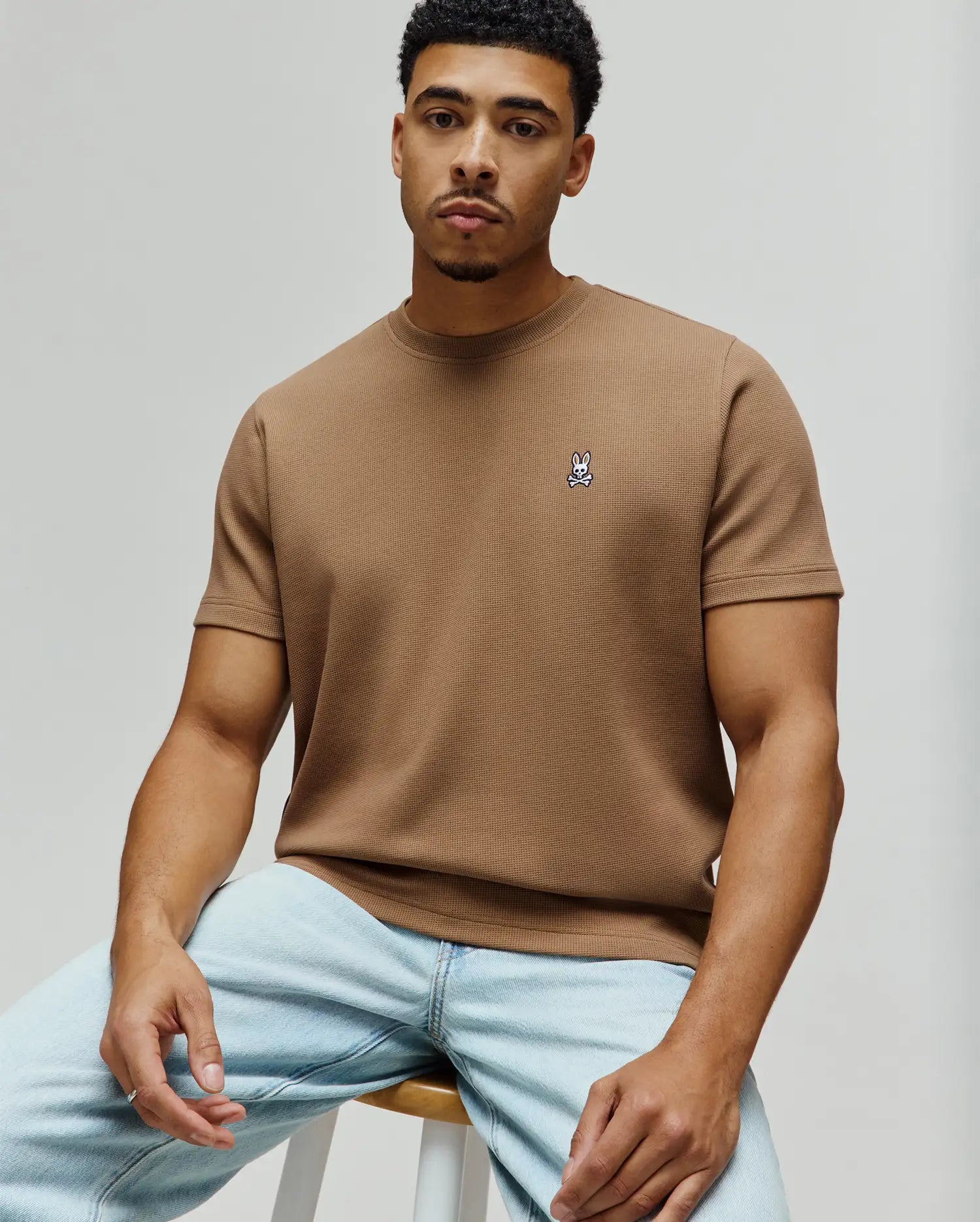 Psycho Bunny Mens Maxton Waffle Tee, a classic fit tan waffle knit t-shirt featuring a small embroidered white and black bunny skull logo on the left chest.