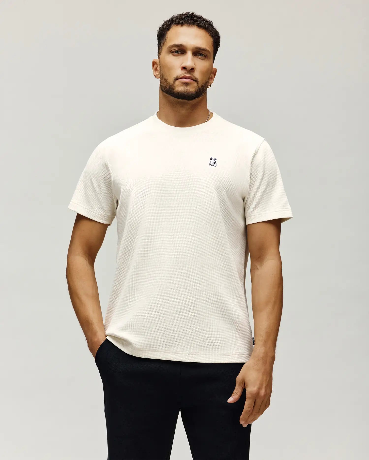Mens Maxton Waffle Tee in cream, featuring a classic fit and textured waffle knit fabric. A small, embroidered Psycho Bunny skull logo in black, white, and blue is on the left chest.